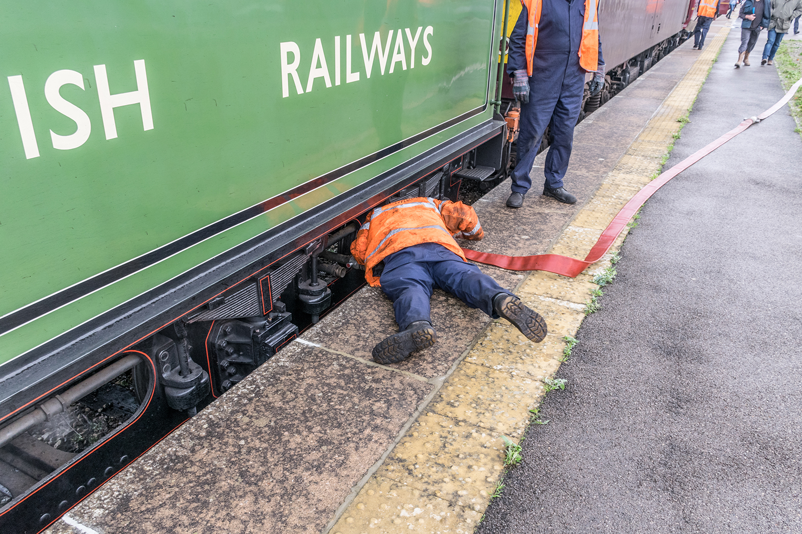 The water tanker's hose is fitted to an inlet point below the tender of the locomotive